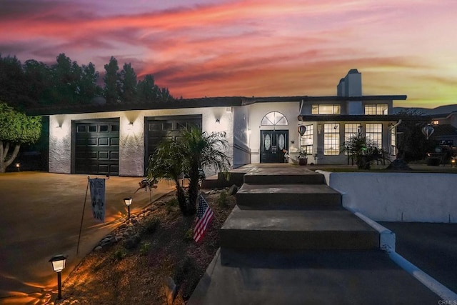 view of front facade featuring french doors, a chimney, stucco siding, a garage, and driveway