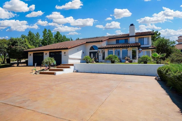 mediterranean / spanish-style house featuring a tiled roof, a chimney, an attached garage, and stucco siding