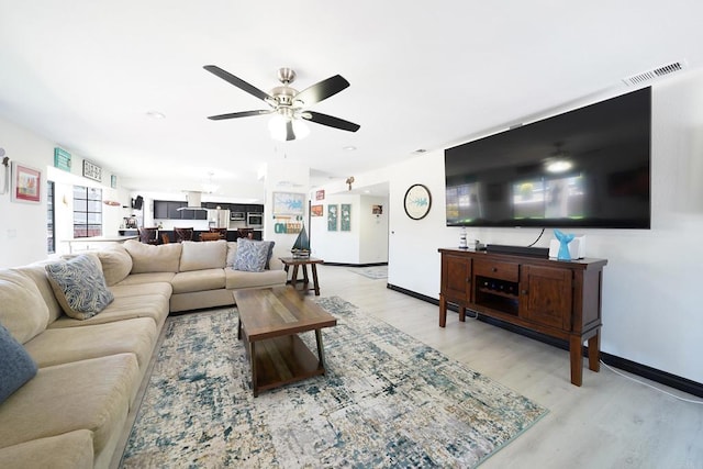 living area featuring baseboards, light wood-type flooring, visible vents, and a ceiling fan