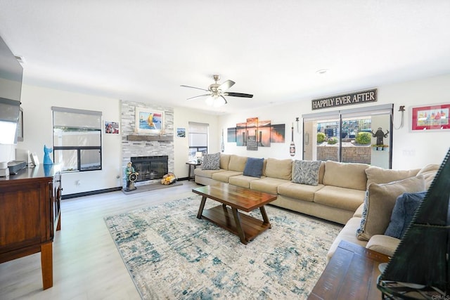 living room with ceiling fan, wood finished floors, and a stone fireplace