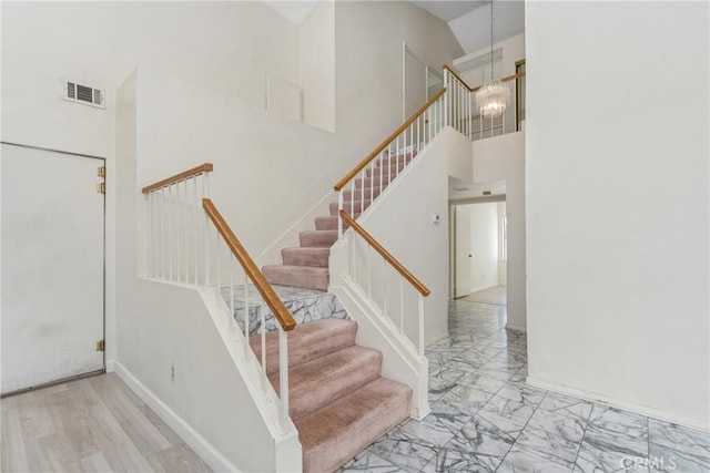 stairway with a notable chandelier, a towering ceiling, visible vents, baseboards, and marble finish floor