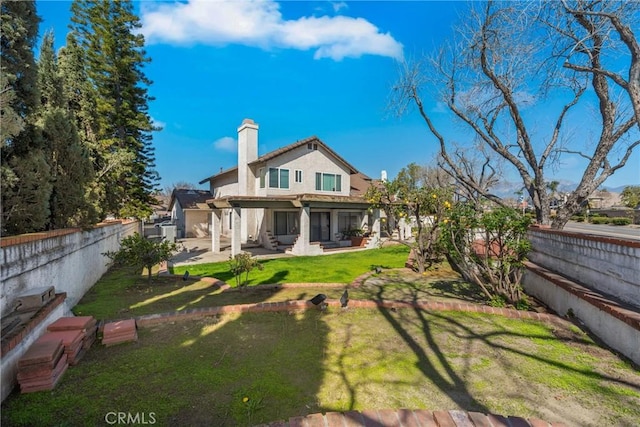 rear view of house featuring a patio, a chimney, a fenced backyard, and a lawn