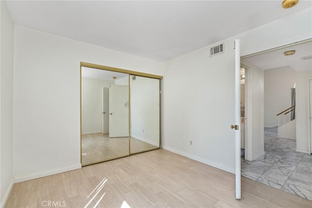 unfurnished bedroom with baseboards, a closet, visible vents, and wood finished floors