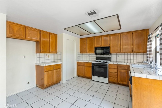 kitchen featuring white gas stove, tile countertops, visible vents, a sink, and black microwave