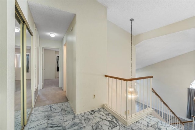 hallway with a textured ceiling, marble finish floor, and an upstairs landing