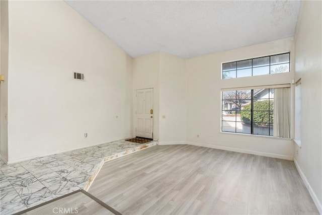 unfurnished room featuring baseboards, visible vents, a towering ceiling, and light wood finished floors