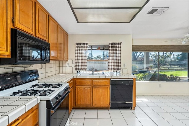 kitchen featuring plenty of natural light, visible vents, tile countertops, black appliances, and a sink