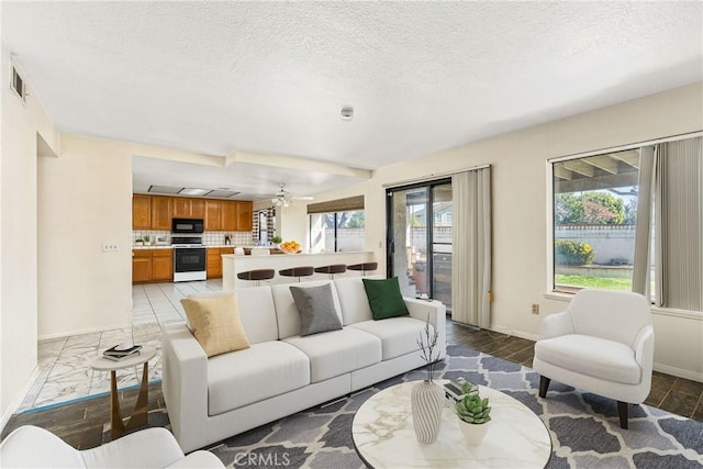 living area featuring baseboards, visible vents, ceiling fan, and a textured ceiling