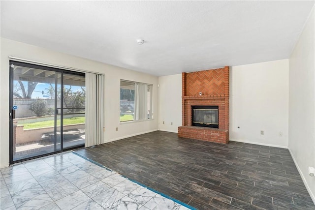 unfurnished living room featuring a brick fireplace, baseboards, and wood finished floors