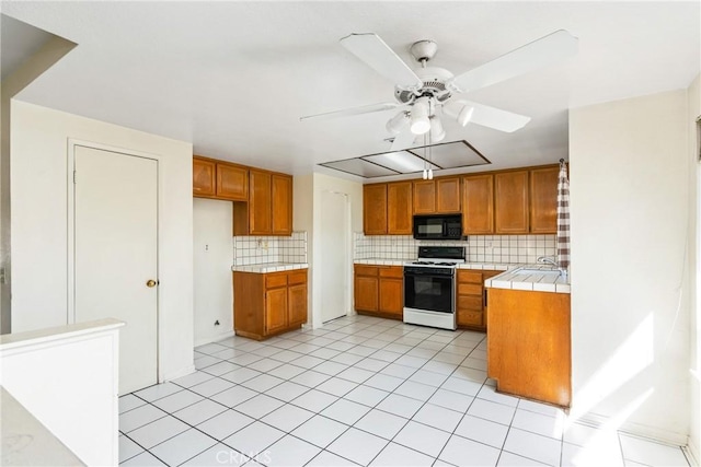 kitchen with black microwave, tile countertops, brown cabinetry, decorative backsplash, and gas range gas stove