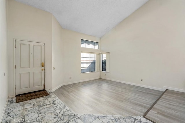 foyer entrance with high vaulted ceiling, baseboards, marble finish floor, and a textured ceiling