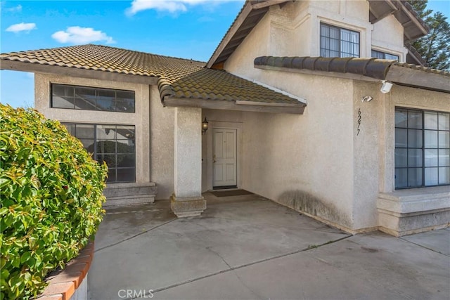 property entrance with a tiled roof, a patio, and stucco siding