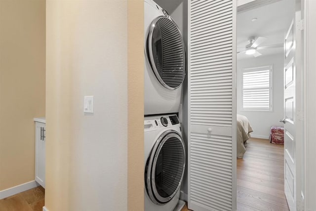 washroom featuring light wood-style flooring, a ceiling fan, stacked washing maching and dryer, baseboards, and laundry area