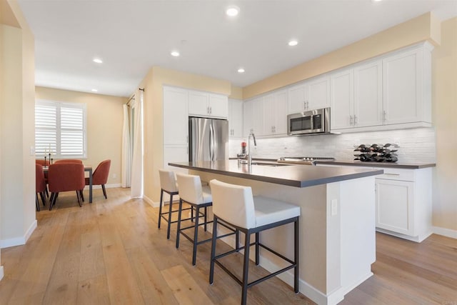 kitchen featuring a sink, tasteful backsplash, dark countertops, appliances with stainless steel finishes, and a breakfast bar area