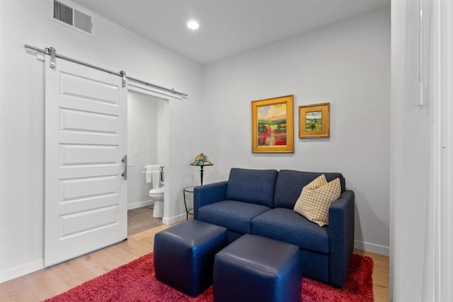 living area with a barn door, light wood-style floors, visible vents, and baseboards