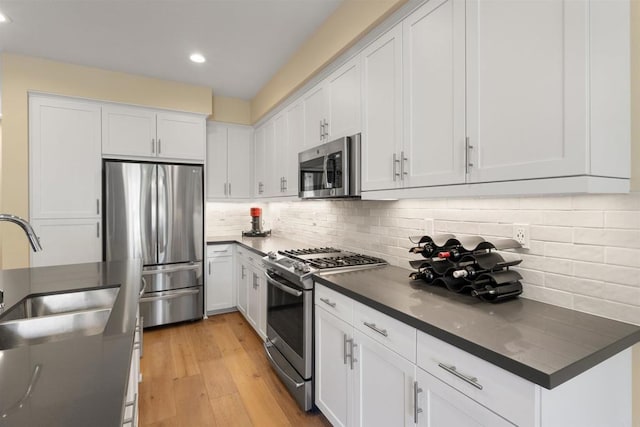 kitchen featuring light wood-style flooring, a sink, decorative backsplash, appliances with stainless steel finishes, and dark countertops