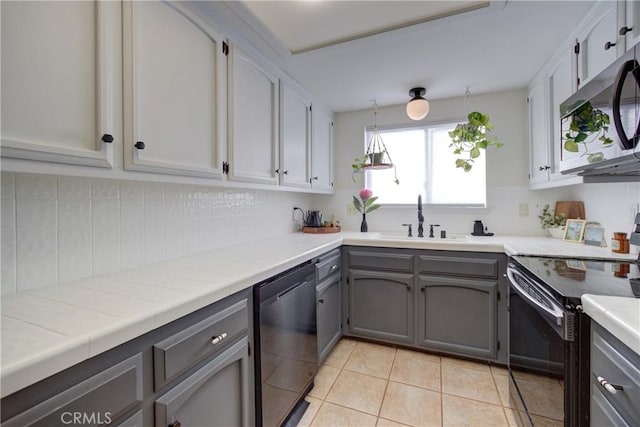 kitchen featuring light tile patterned floors, tasteful backsplash, gray cabinetry, a sink, and black appliances