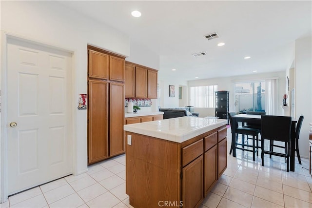 kitchen with brown cabinetry, visible vents, tile countertops, and light tile patterned flooring