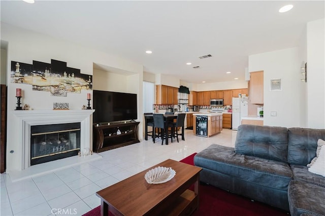 living room featuring light tile patterned floors, recessed lighting, visible vents, and a glass covered fireplace