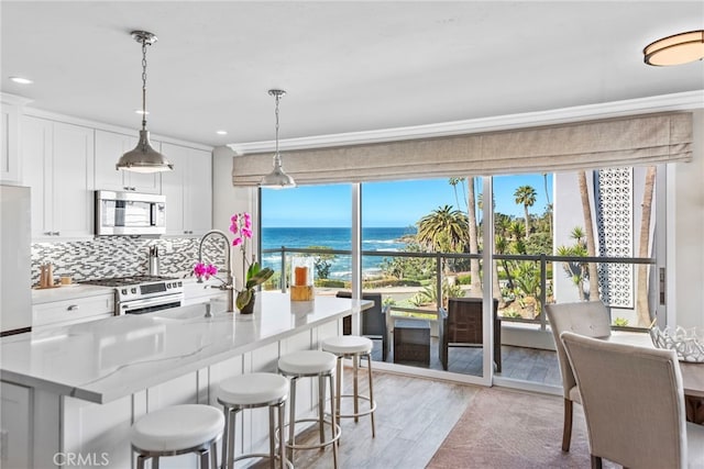 kitchen featuring backsplash, a water view, stainless steel appliances, white cabinetry, and a sink