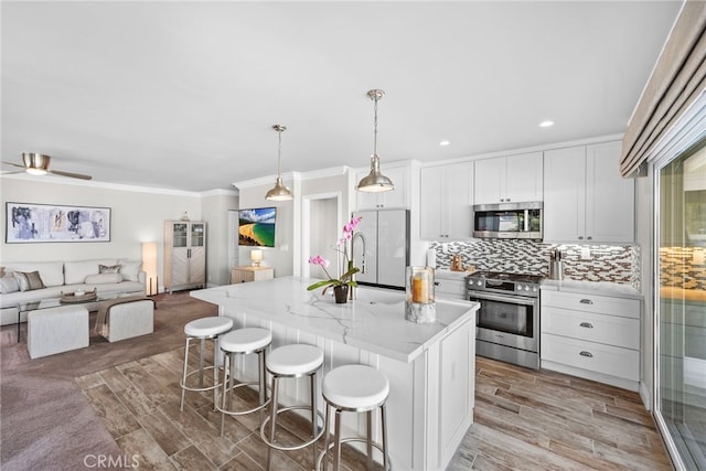 kitchen featuring stainless steel appliances, a breakfast bar, white cabinets, open floor plan, and decorative backsplash