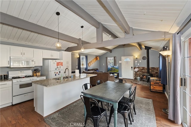 kitchen with lofted ceiling with beams, dark wood-type flooring, a wood stove, open floor plan, and white appliances