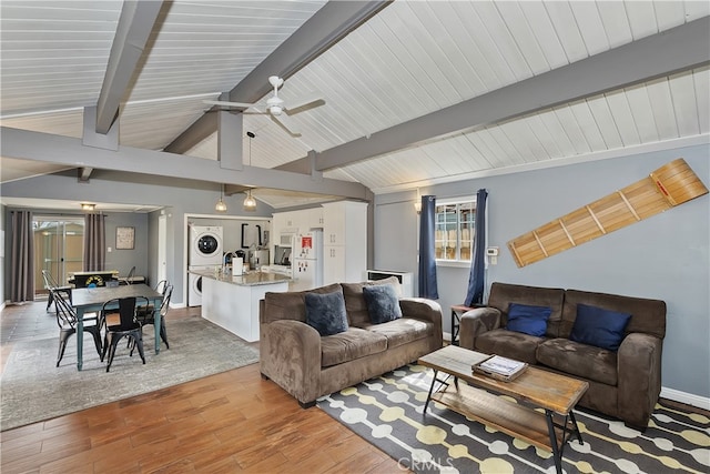 living area featuring stacked washer and dryer, baseboards, ceiling fan, vaulted ceiling with beams, and light wood-style floors