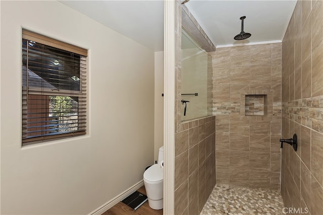 full bathroom featuring toilet, baseboards, a tile shower, and crown molding