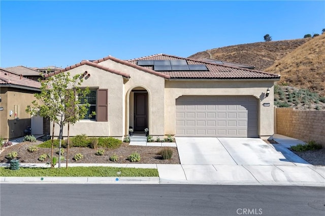 mediterranean / spanish-style home with a garage, solar panels, concrete driveway, a tile roof, and stucco siding