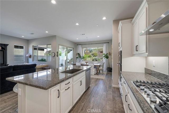 kitchen with stainless steel appliances, recessed lighting, dark wood-type flooring, a sink, and wall chimney exhaust hood