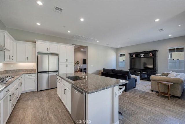 kitchen featuring open floor plan, stainless steel appliances, light wood-type flooring, and a sink