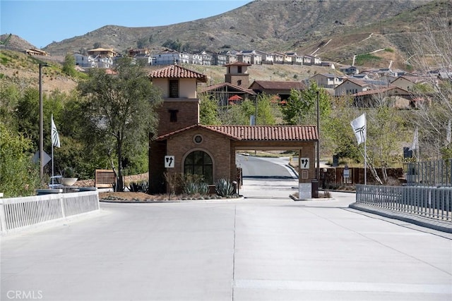 mediterranean / spanish house with concrete driveway, a tile roof, a mountain view, and fence