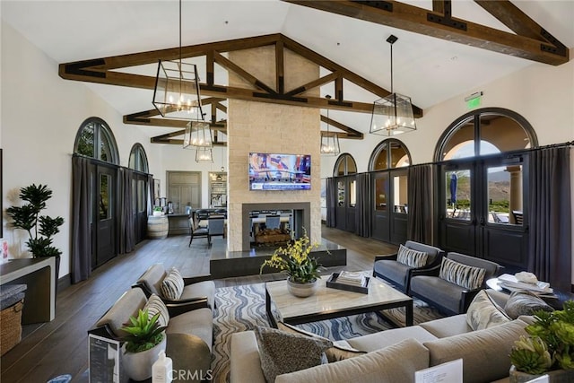 living area featuring wood-type flooring, a tiled fireplace, a notable chandelier, and beamed ceiling