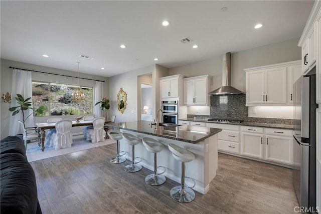 kitchen with wall chimney range hood, dark wood-type flooring, appliances with stainless steel finishes, and tasteful backsplash