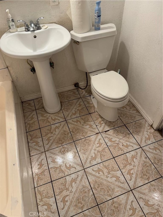 bathroom featuring toilet, a textured wall, baseboards, and tile patterned floors