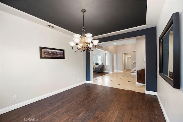 spare room featuring a raised ceiling, visible vents, baseboards, and wood finished floors