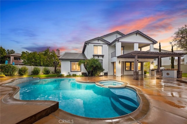 pool at dusk with a patio area, fence, a pool with connected hot tub, and a pergola