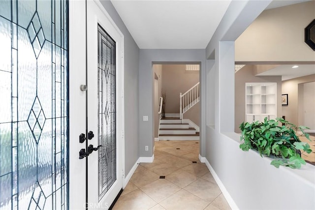 foyer entrance featuring light tile patterned flooring, baseboards, and stairs