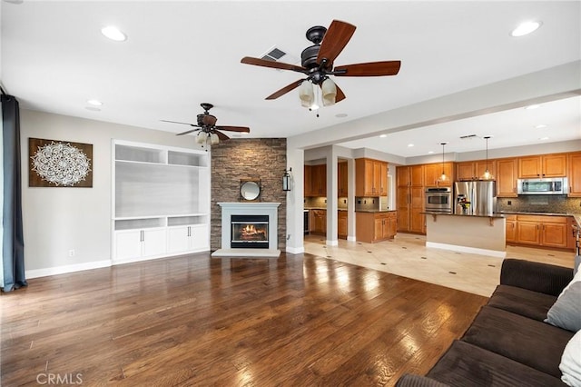 living area with recessed lighting, visible vents, light wood-style floors, a stone fireplace, and baseboards