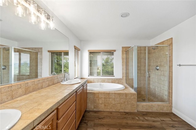 bathroom featuring double vanity, wood finished floors, a stall shower, and a sink