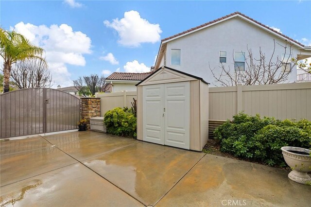 view of patio with fence private yard, a gate, an outdoor structure, and a shed