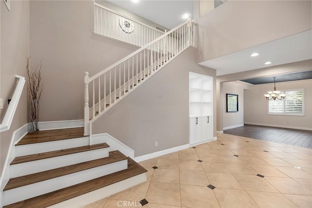 stairway featuring a notable chandelier, tile patterned floors, a towering ceiling, and baseboards