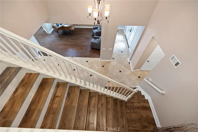 stairway featuring visible vents, a notable chandelier, baseboards, and wood finished floors