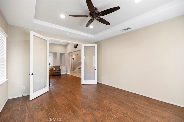 spare room featuring a tray ceiling, french doors, visible vents, wood finished floors, and baseboards