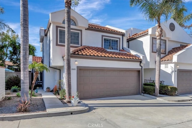 mediterranean / spanish-style home with driveway, an attached garage, a tile roof, and stucco siding