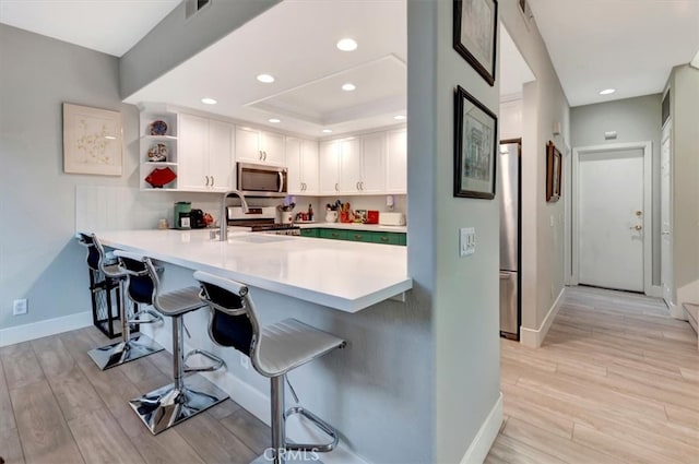 kitchen with stainless steel appliances, a breakfast bar area, a raised ceiling, and light wood-style flooring