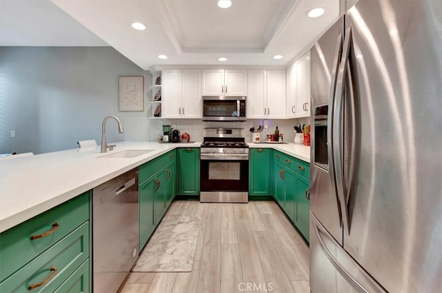 kitchen featuring appliances with stainless steel finishes, a tray ceiling, green cabinetry, and a sink