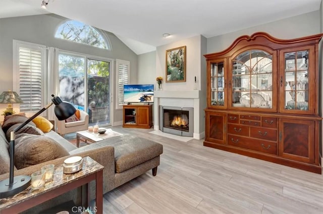 living room with vaulted ceiling, a fireplace with flush hearth, and light wood-style floors