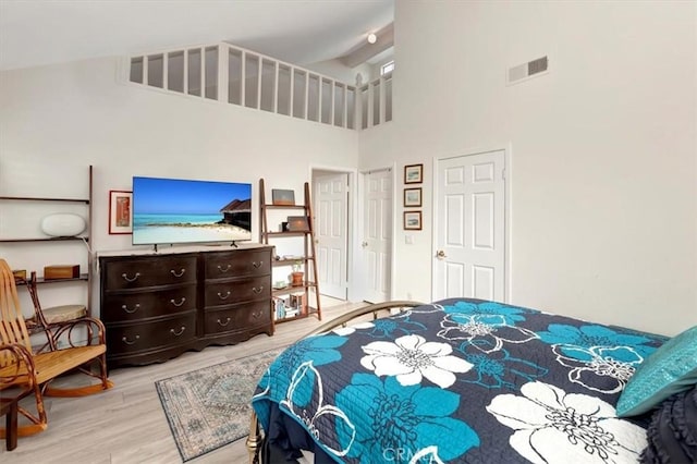 bedroom featuring high vaulted ceiling, light wood-type flooring, and visible vents