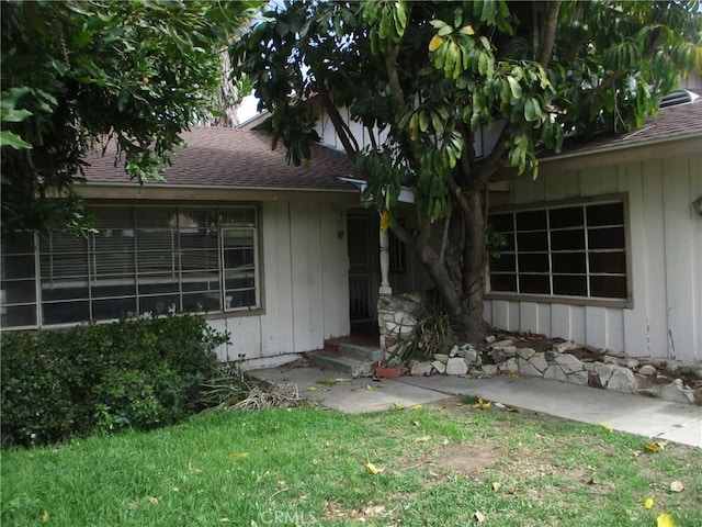 exterior space featuring board and batten siding, a lawn, and roof with shingles